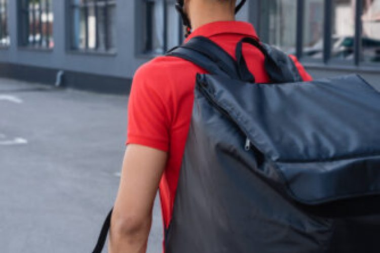 Back view of courier in helmet and thermo backpack standing outdoors